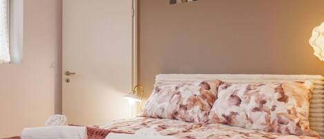 Ein Schlafzimmer mit einem Bett, zwei Handtüchern, einem Nachttisch, einer Lampe und einem an der Wand befestigten Regal mit Uhren.