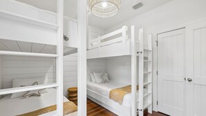 A room with bunk beds, a wooden floor, a white door, and a hanging light fixture. - Magnolia Cottages on 30A: 5-Min Walk to the Beach! 2 King Beds, Bunk Room (Inlet Beach)