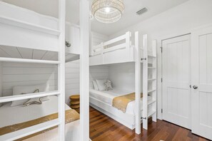 A room with bunk beds, a wooden floor, a white door, and a hanging light fixture. - Magnolia Cottages on 30A: 5-Min Walk to the Beach! 2 King Beds, Bunk Room (Inlet Beach)