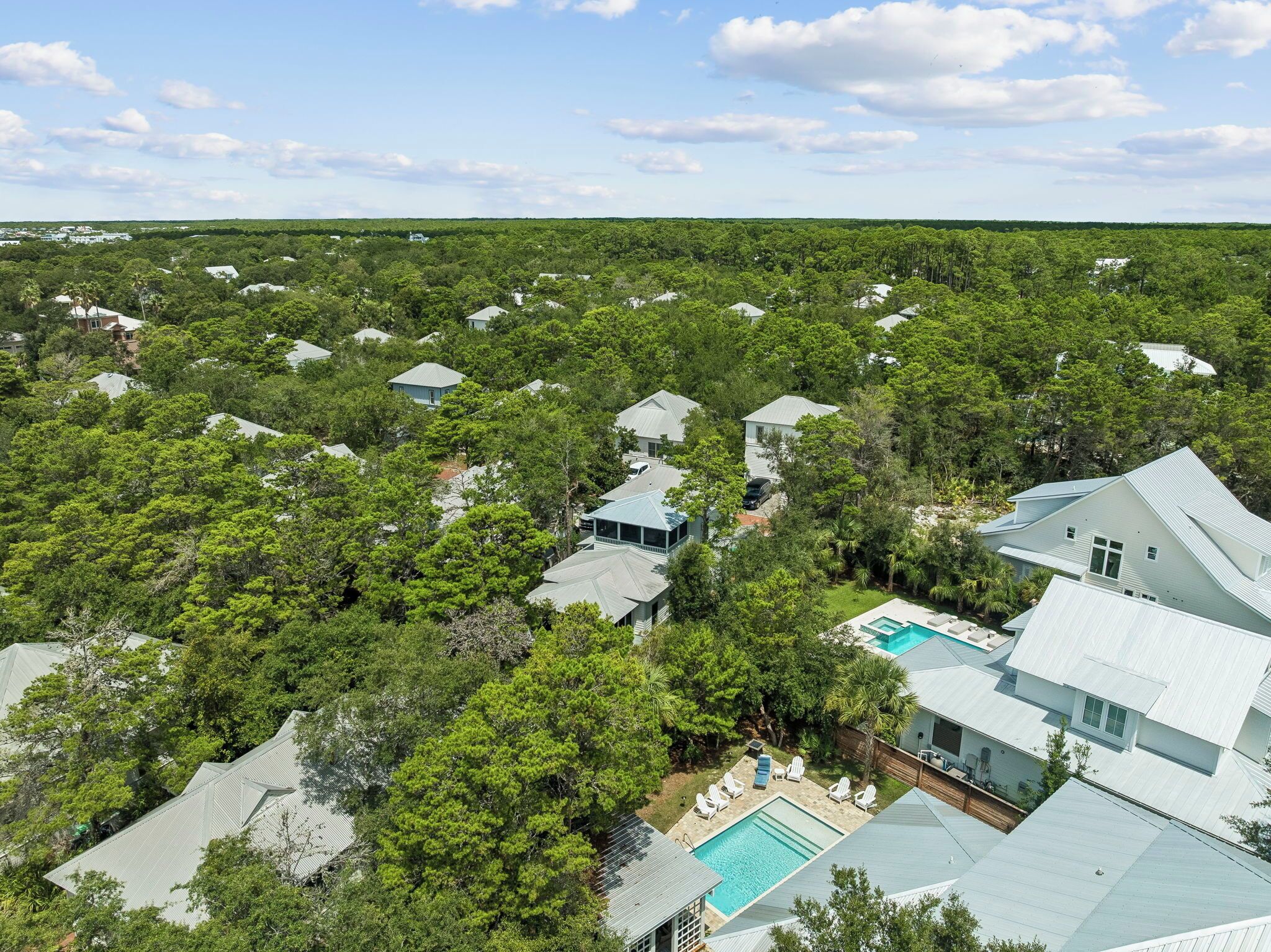 Et boligområde med flere huse omgivet af frodig vegetation, en swimmingpool og en klar himmel.