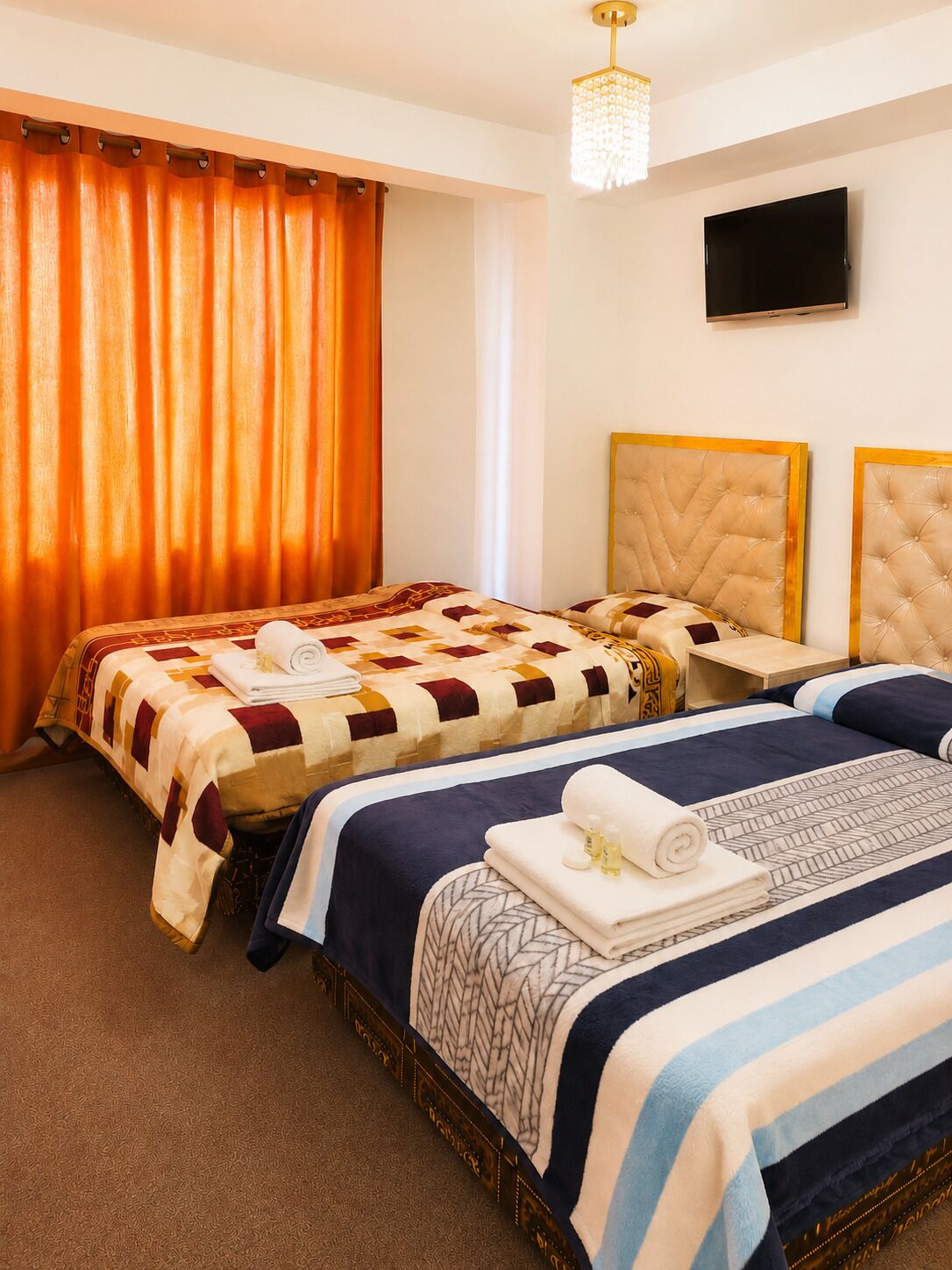 A hotel room with two beds, a flat-screen TV, and a chandelier.