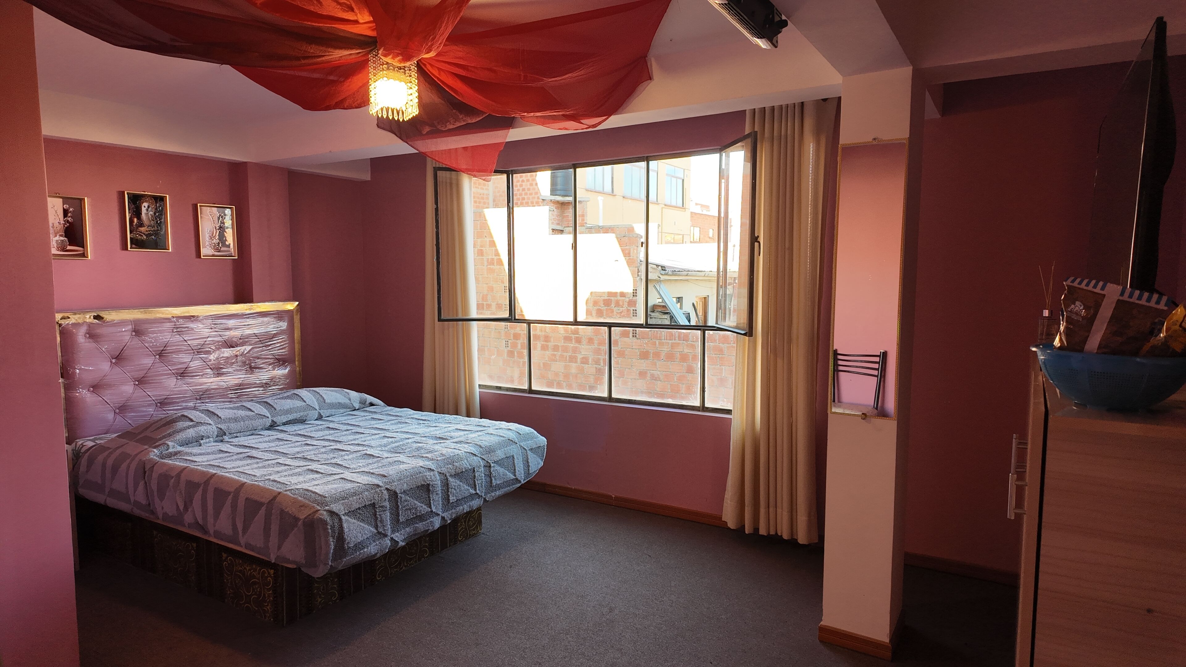 Un dormitorio con cama, ventana y vista a edificios.
