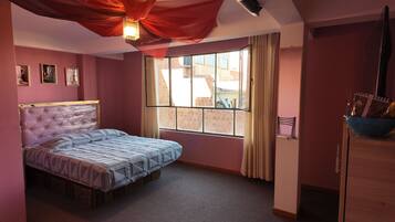 Un dormitorio con cama, ventana y vista a edificios.