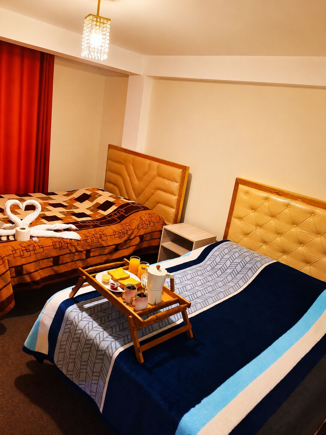 Una camera d'albergo con due letti, un tavolino in legno con articoli per la colazione e un lampadario.
