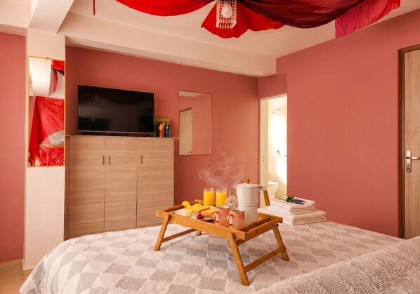 Habitación de hotel con cama, televisor, armario, bandeja de desayuno y zona de ducha.