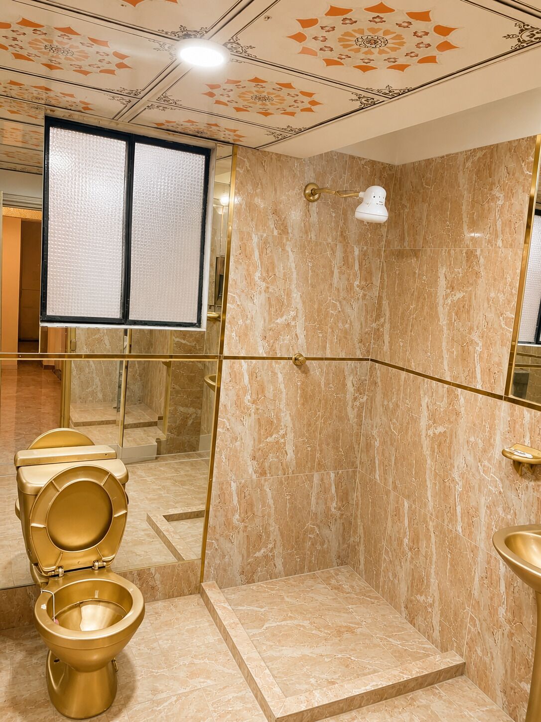 A bathroom with a marble floor, a shower with a gold frame, and a toilet with a gold seat.