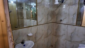 A bathroom with marble walls, a sink, a mirror, and a shower area.