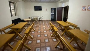 A room with multiple wooden tables and chairs, a flat-screen TV mounted on the wall, and patterned flooring.