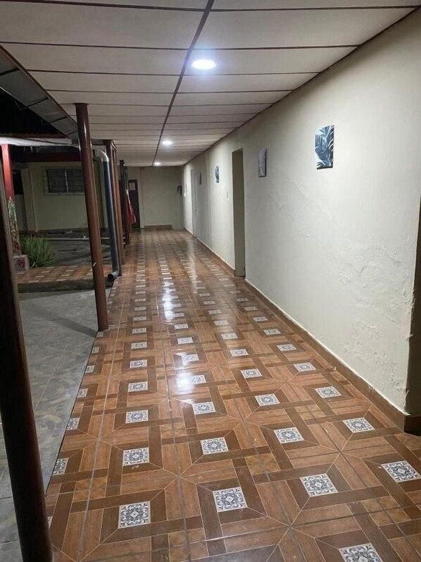 A corridor with patterned flooring, a ceiling with recessed lighting, and a wall-mounted logo.