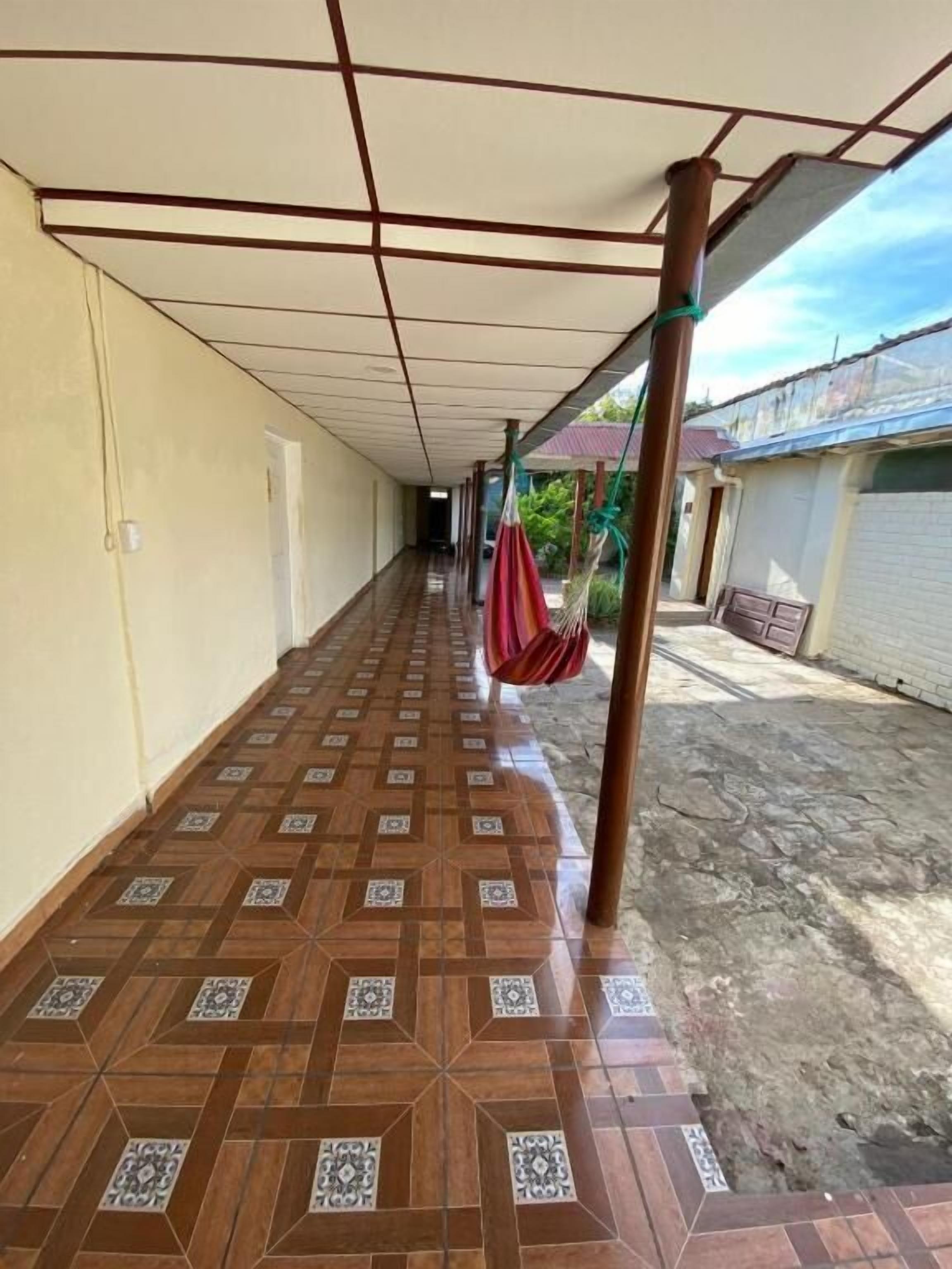 Un corredor techado con piso estampado, una hamaca colgante y una estructura de postes metálicos.