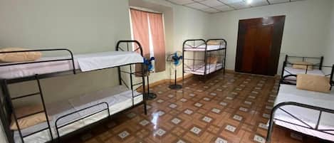 A dormitory room with bunk beds, a window with curtains, a door, and a patterned floor.