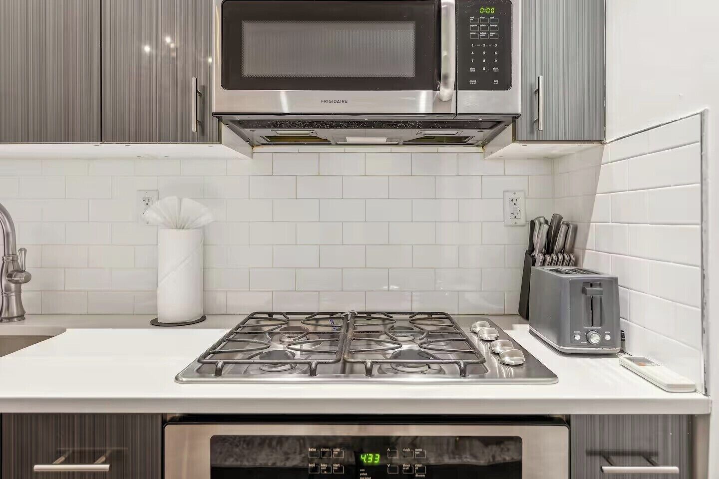 A kitchen with a stainless steel microwave, a gas stove, and a toaster.