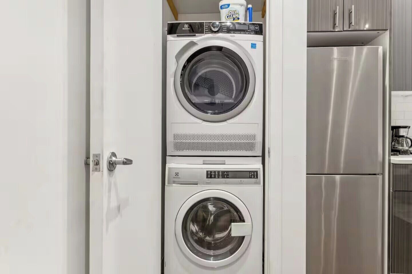 A compact laundry area with two front-loading washing machines and a stainless steel refrigerator.
