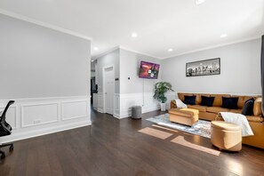 Ein modernes Wohnzimmer mit einer Couch, einem Hocker und einem flachbildfernseher an der Wand.