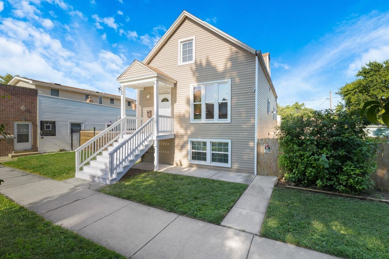 A two-story residential building with a front porch, a staircase, and a small front yard.