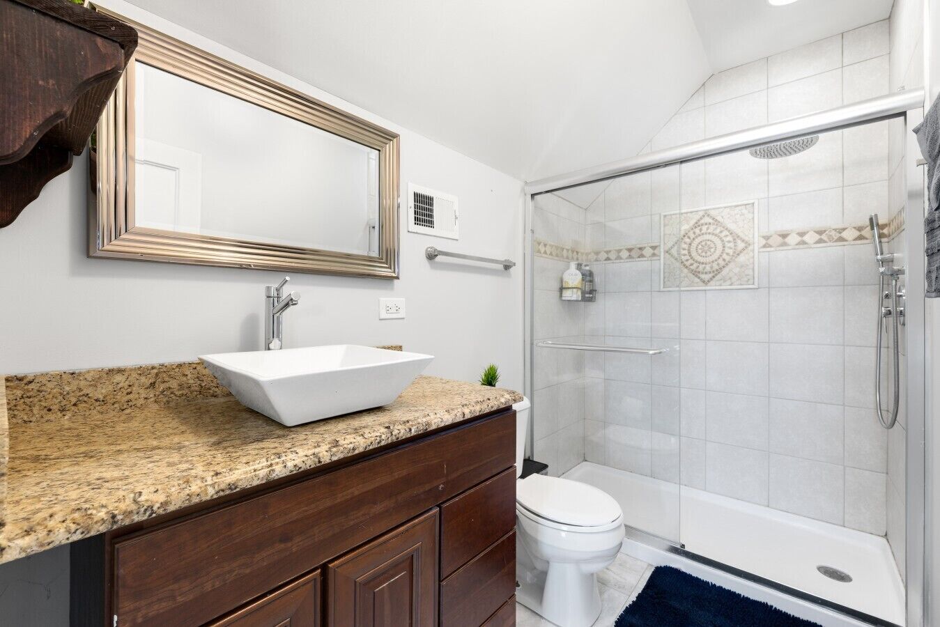 A bathroom with a white sink, dark wooden vanity, a large mirror, a toilet, and a glass-enclosed shower area.