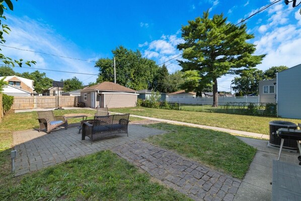 Ein Hinterhof mit einer gepflasterten Terrasse, einer Holzbank und einem kleinen Gartenhaus.