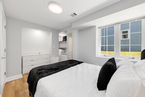 Ein Schlafzimmer mit einem Bett, einem Kleiderschrank, einem Spiegel und einem Fenster mit Blick auf ein Haus.