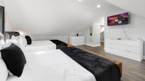 Una camera da letto moderna con due letti, una cassettiera bianca, una TV a muro e un pavimento in legno.