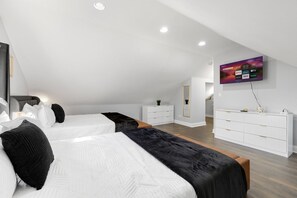 Ein modernes Schlafzimmer mit zwei Betten, einer weißen Kommode, einem an der Wand montierten Fernseher und Holzboden.