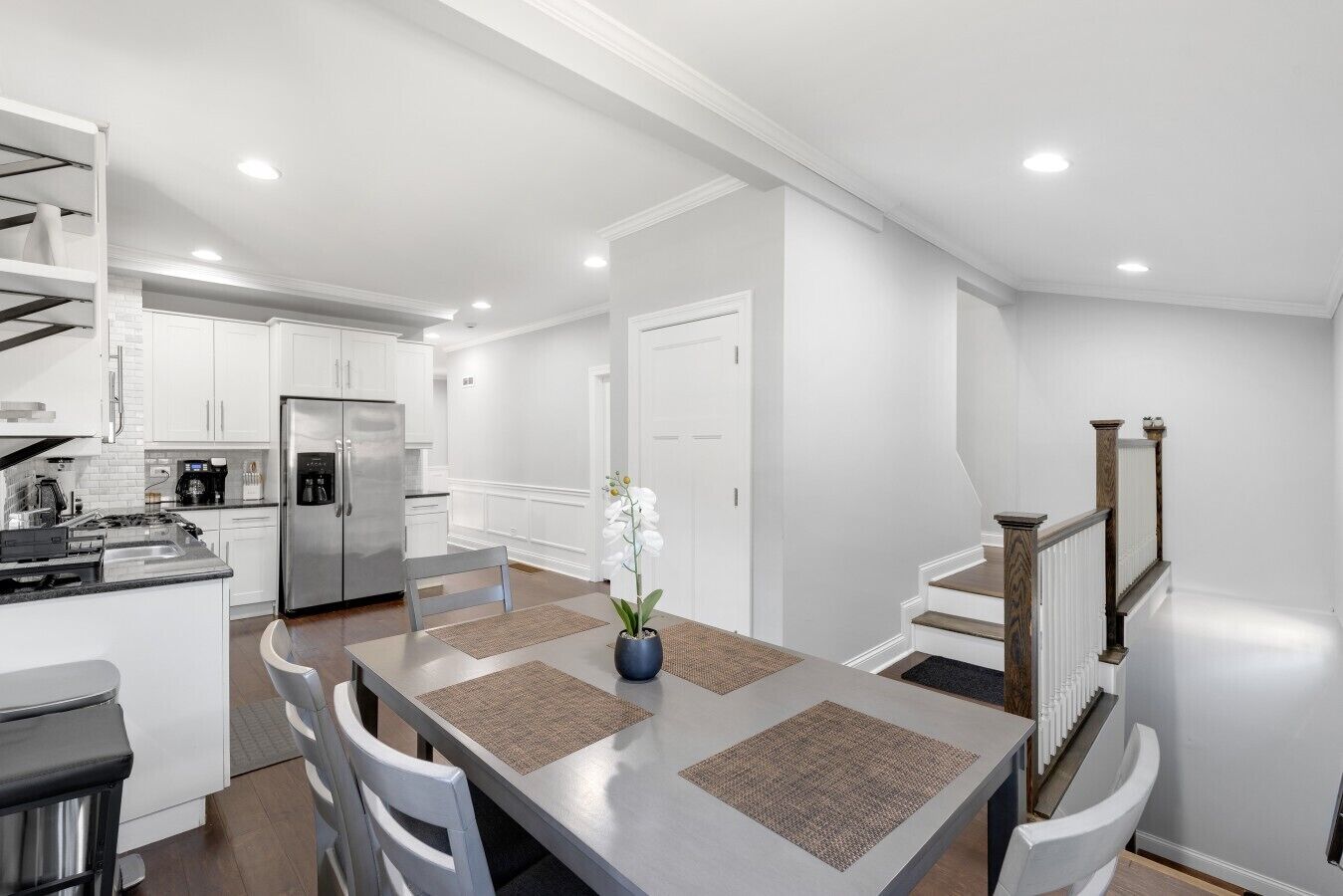A modern kitchen with white cabinetry, a stainless steel refrigerator, and a dining area with a table and chairs.