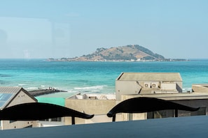 A coastal view with a hill in the distance, a pier, and buildings with a flat roof.