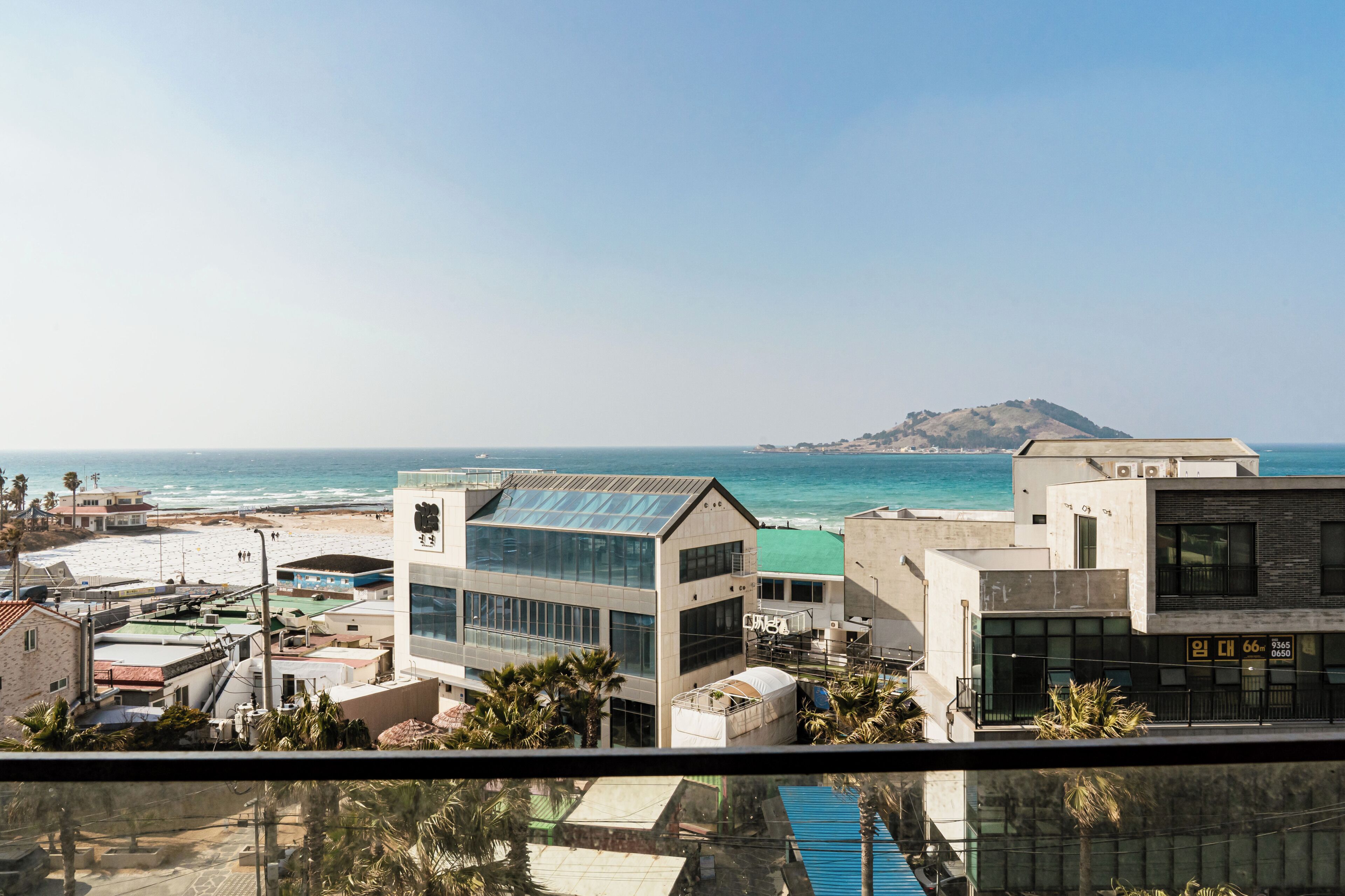 Vista costera con edificios modernos, una playa y una colina distante.