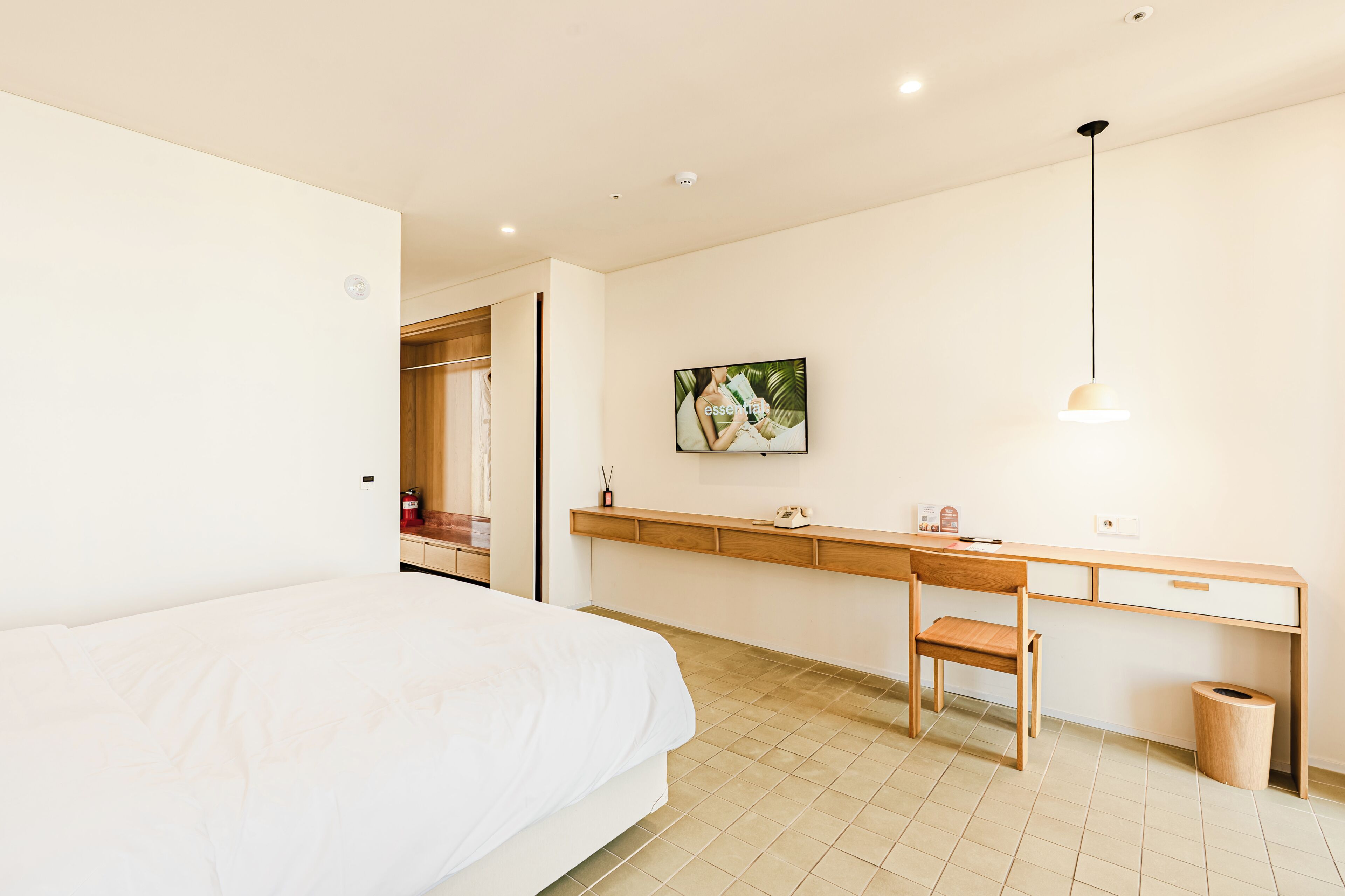 A bedroom with a bed, a desk, a chair, a waste bin, and a painting on the wall.