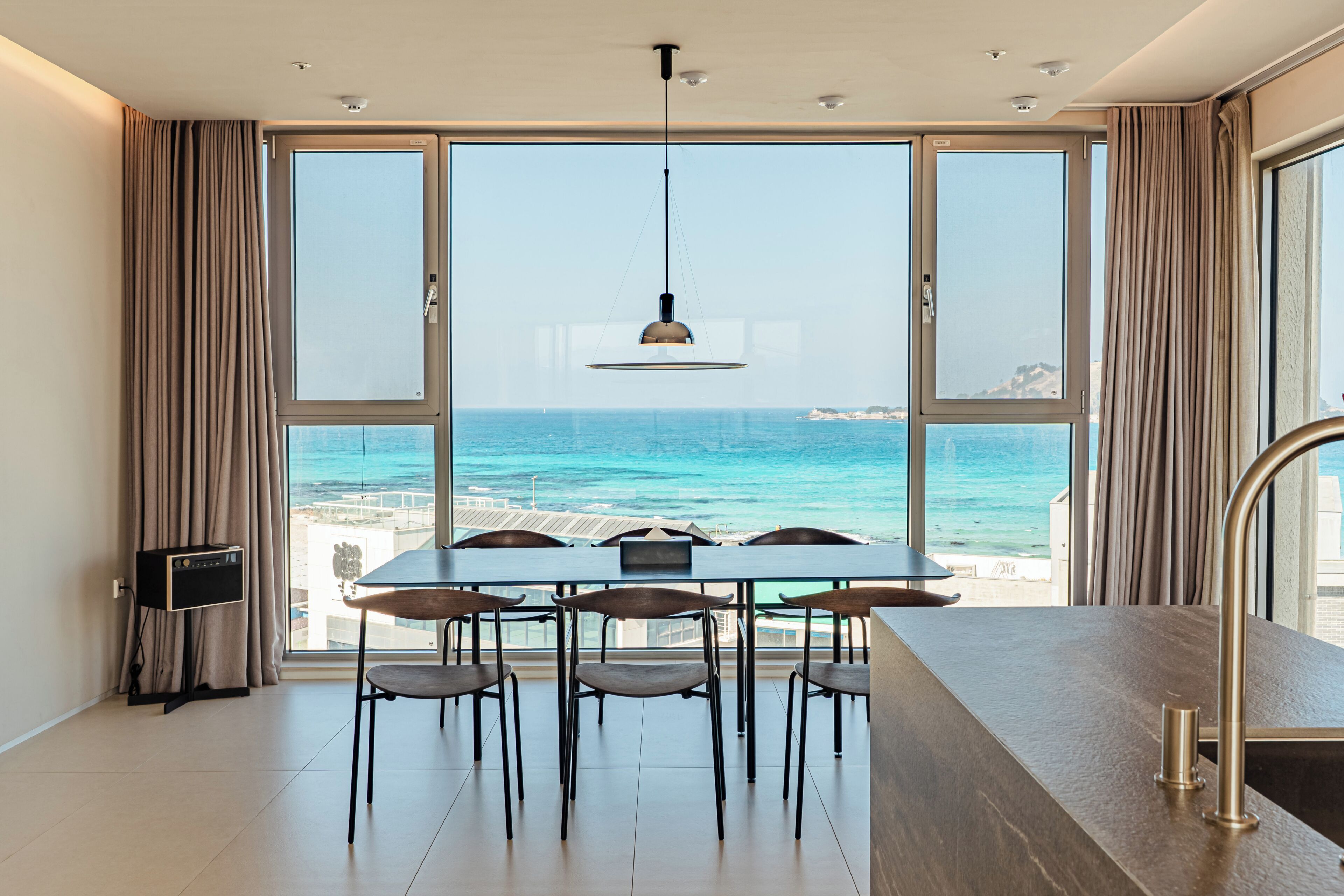 Un espace repas avec vue sur la mer, comprenant une table, des chaises et un luminaire suspendu.