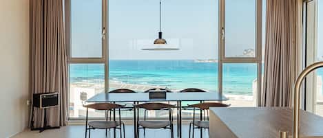 A dining area with a view of the sea, a table, chairs, and a pendant light.