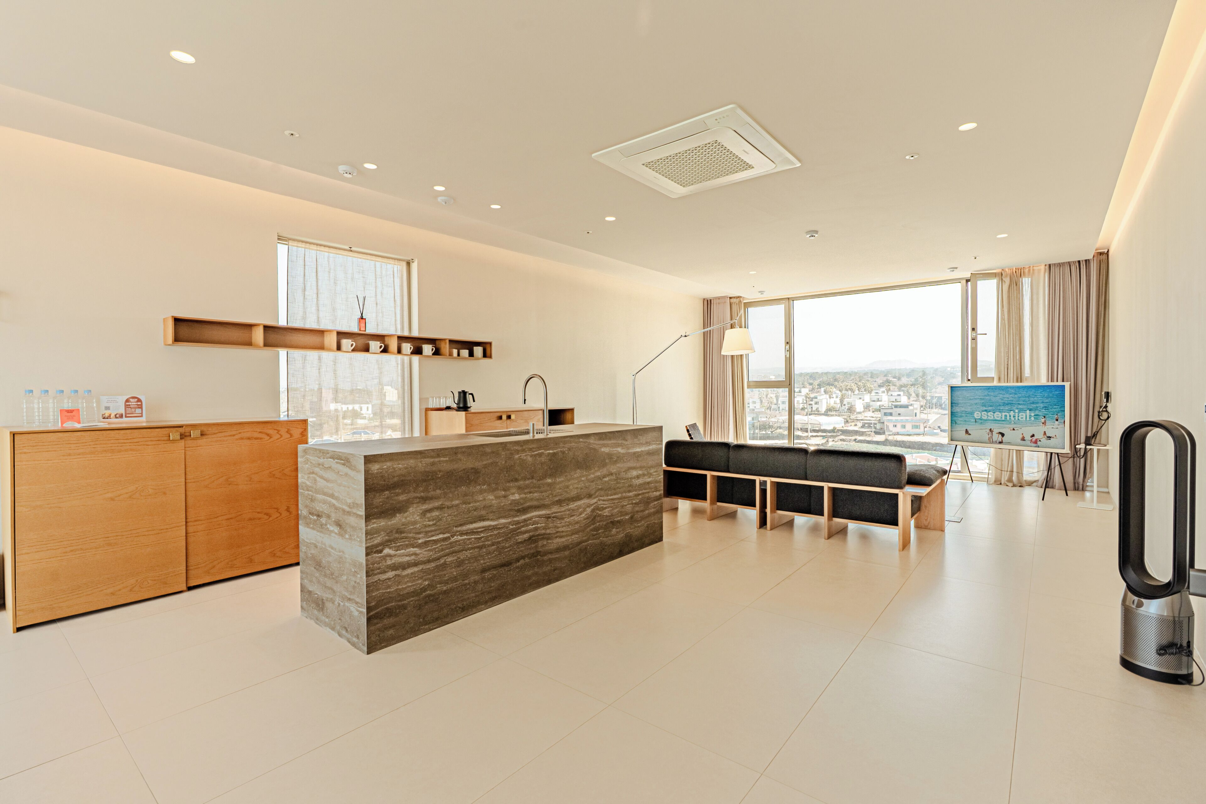 A modern hotel room with a kitchen area, a seating area with a view, and a large window.