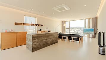 A modern hotel room with a kitchen area, a seating area with a view, and a large window.