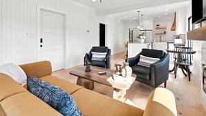 A modern living room with a chandelier, sofas, and a coffee table. - Historic Swansboro Retreat- 3-bedrooms- Water Views & Spa Bath (Swansboro)