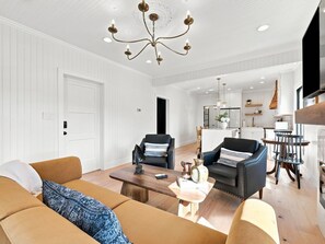 A modern living room with a chandelier, sofas, and a coffee table. - Historic Swansboro Retreat- 3-bedrooms- Water Views & Spa Bath (Swansboro)