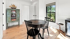 A dining area with a wooden table and chairs, a ceiling fan, a bookshelf, and a window with a view of greenery. - Historic Swansboro Retreat- 3-bedrooms- Water Views & Spa Bath (Swansboro)