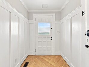 A hallway with a white door, a window with a view, and a doorbell. - Historic Swansboro Retreat- 3-bedrooms- Water Views & Spa Bath (Swansboro)