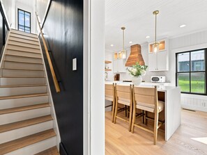 A modern kitchen with a central island, pendant lighting, and a view of the outdoors through large windows. - Historic Swansboro Retreat- 3-bedrooms- Water Views & Spa Bath (Swansboro)