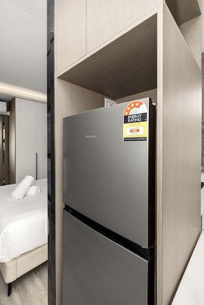 A modern hotel room with a built-in refrigerator, a bed with white linens, and a visible energy efficiency rating sticker.