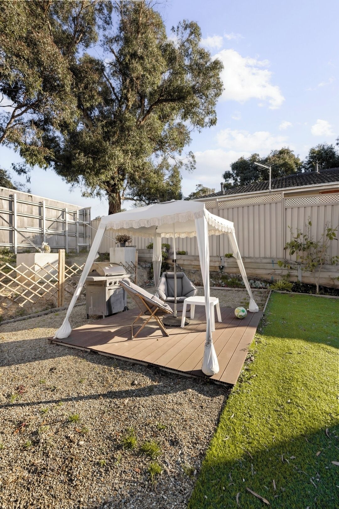 A covered outdoor seating area with a grill, lounge chairs, and a small table.