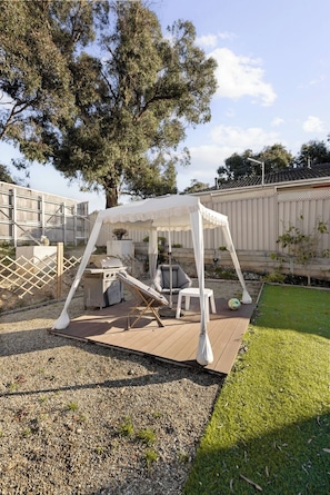 A covered outdoor seating area with a grill, lounge chairs, and a small table.