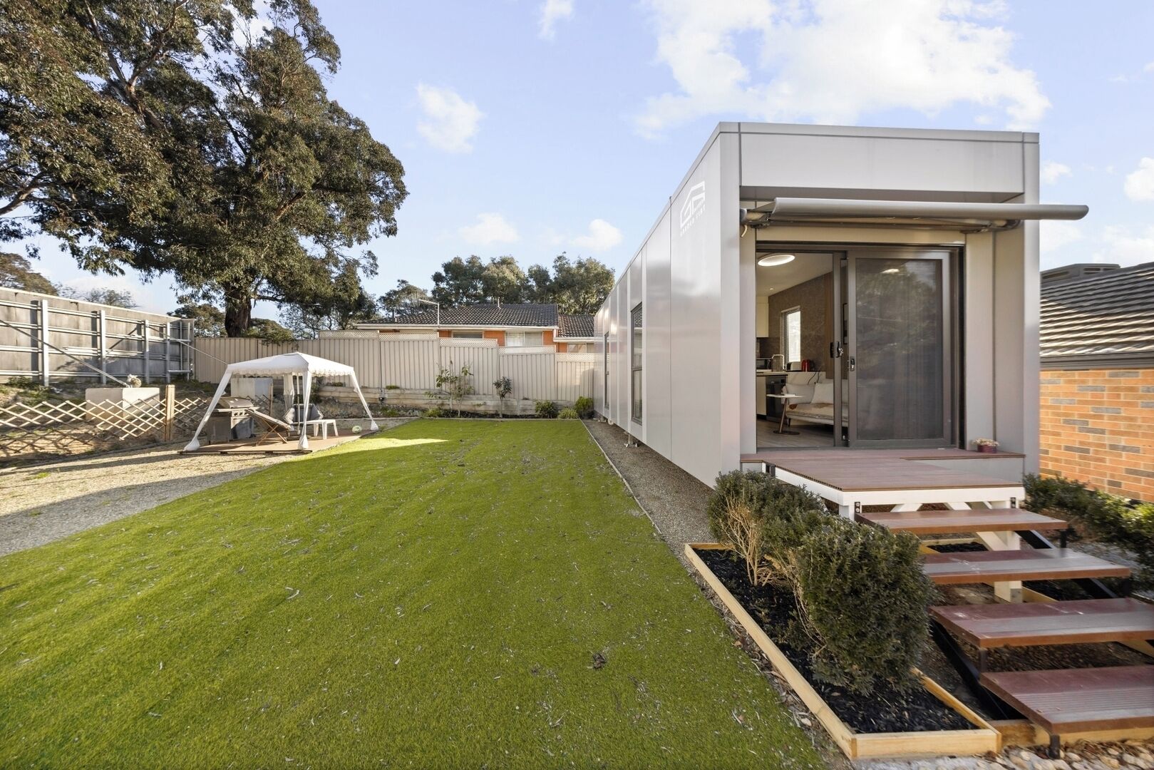 Une maison moderne dotée d’une pelouse bien entretenue, d’un espace extérieur couvert aménagé en salon et d’une cuisine ouverte.