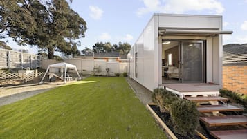 A modern house with a well-maintained lawn, a covered outdoor seating area, and a visible kitchen.