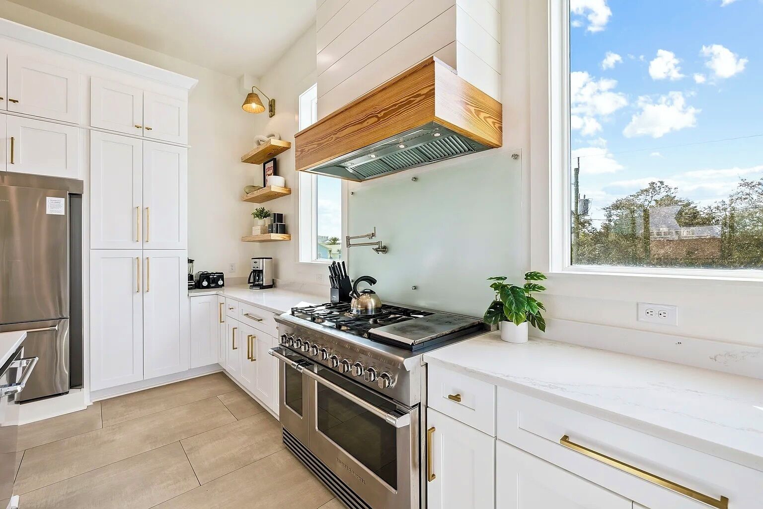 A modern kitchen with white cabinetry, stainless steel appliances, and a large window providing a view of the outdoors.