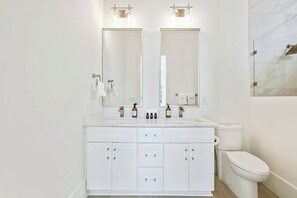 Un bagno moderno con un mobile lavabo bianco, due specchi, un WC e uno spazio doccia.