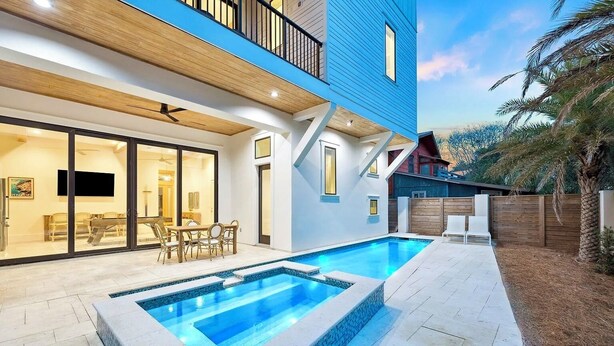 Ein modernes Haus mit Swimmingpool, einem Essbereich mit Gartenmöbeln und einem großen Fenster mit Blick auf den Pool.
