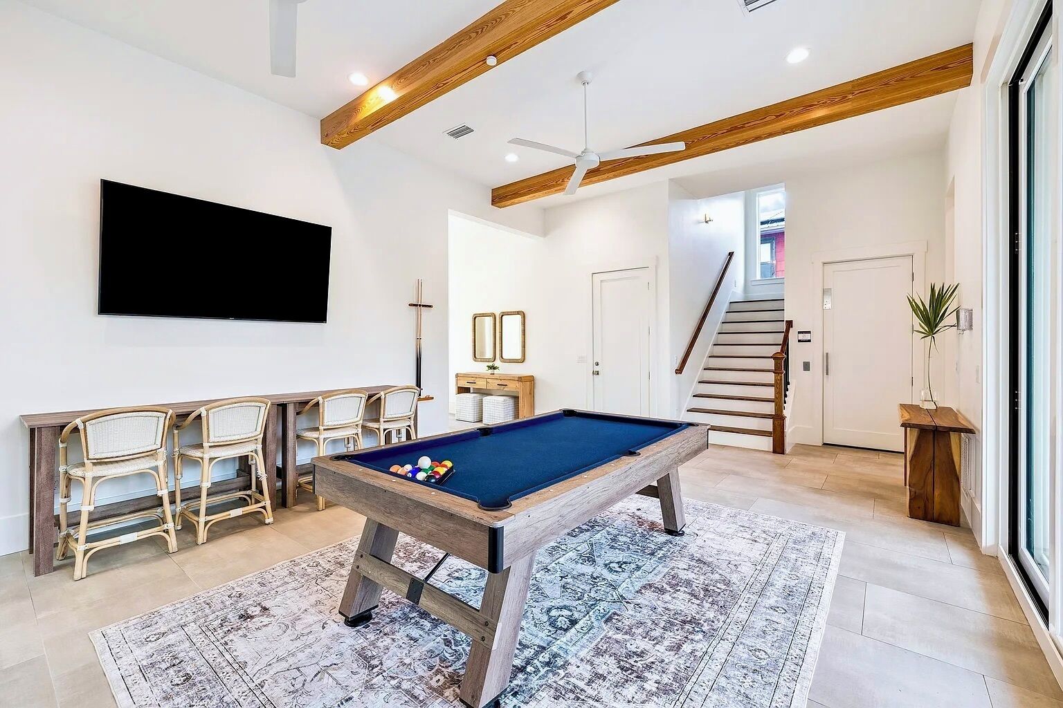 A modern living room with a pool table, seating area, and a staircase leading to another level.