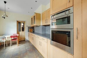 Eine Küche mit Holzausstattung, einem Edelstahlbackofen und einem Essbereich mit Tisch und Stühlen.