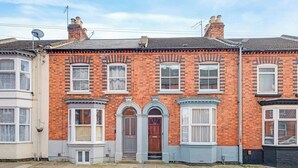 A red brick terraced house with bay windows, a front door, and a small porch. - 3BR Victorian Home for Up to 5 Guests (West Northamptonshire)