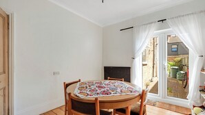 A room with a round wooden table, four chairs, a radiator, and a view of a garden through a glass door. - 3BR Victorian Home for Up to 5 Guests (West Northamptonshire)