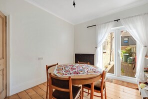 Ein Zimmer mit einem runden Holztisch, vier Stühlen, einer Heizung und Blick auf einen Garten durch eine Glastür.